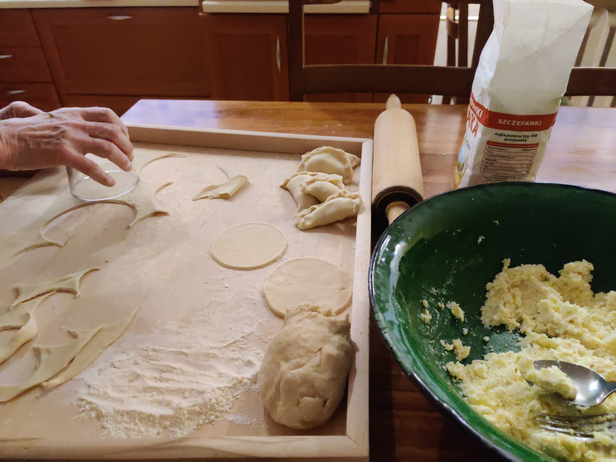 na zdjęciu: po lewej ciasto na pierogi, wycinanie okręgów, po prawej mąka, wałek, miska z farszem (twaróg, ziemniaki, sól, pieprz, cebula)